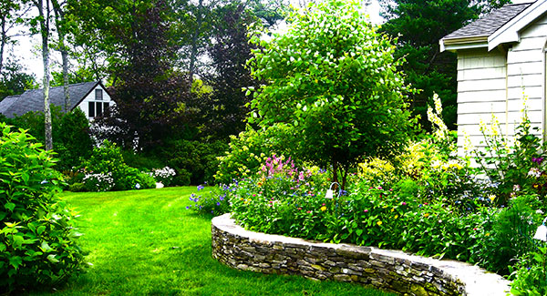 Landscaping and yard maintenance services. Beautiful curved rock wall with plants and shrubs.